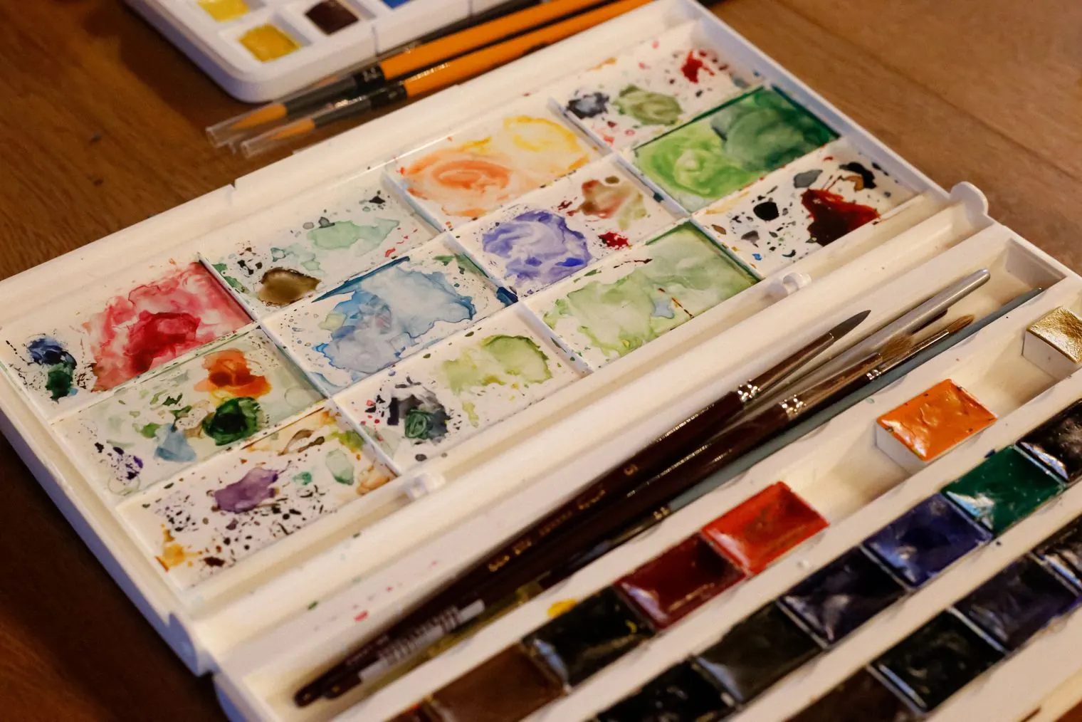 A watercolor paint set with brushes on a wooden table