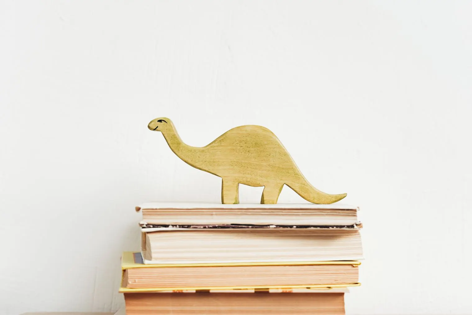 A wooden toy dinosaur standing on a stack of books