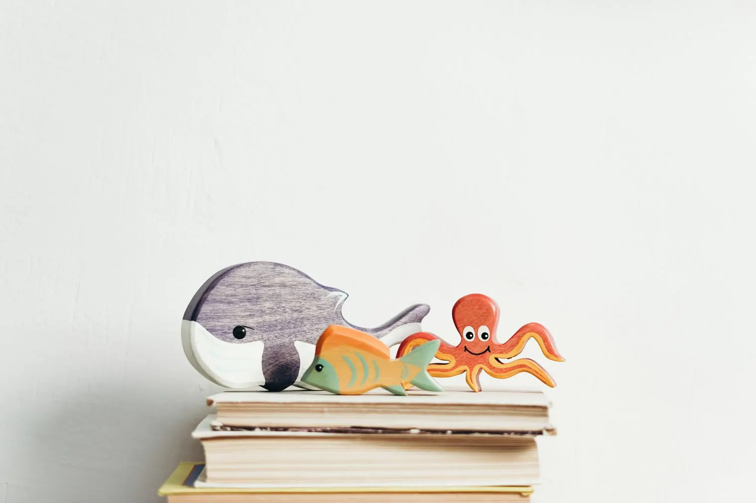 Wooden toy sea animals, a whale, a fish and an octopus, on a stack of books
