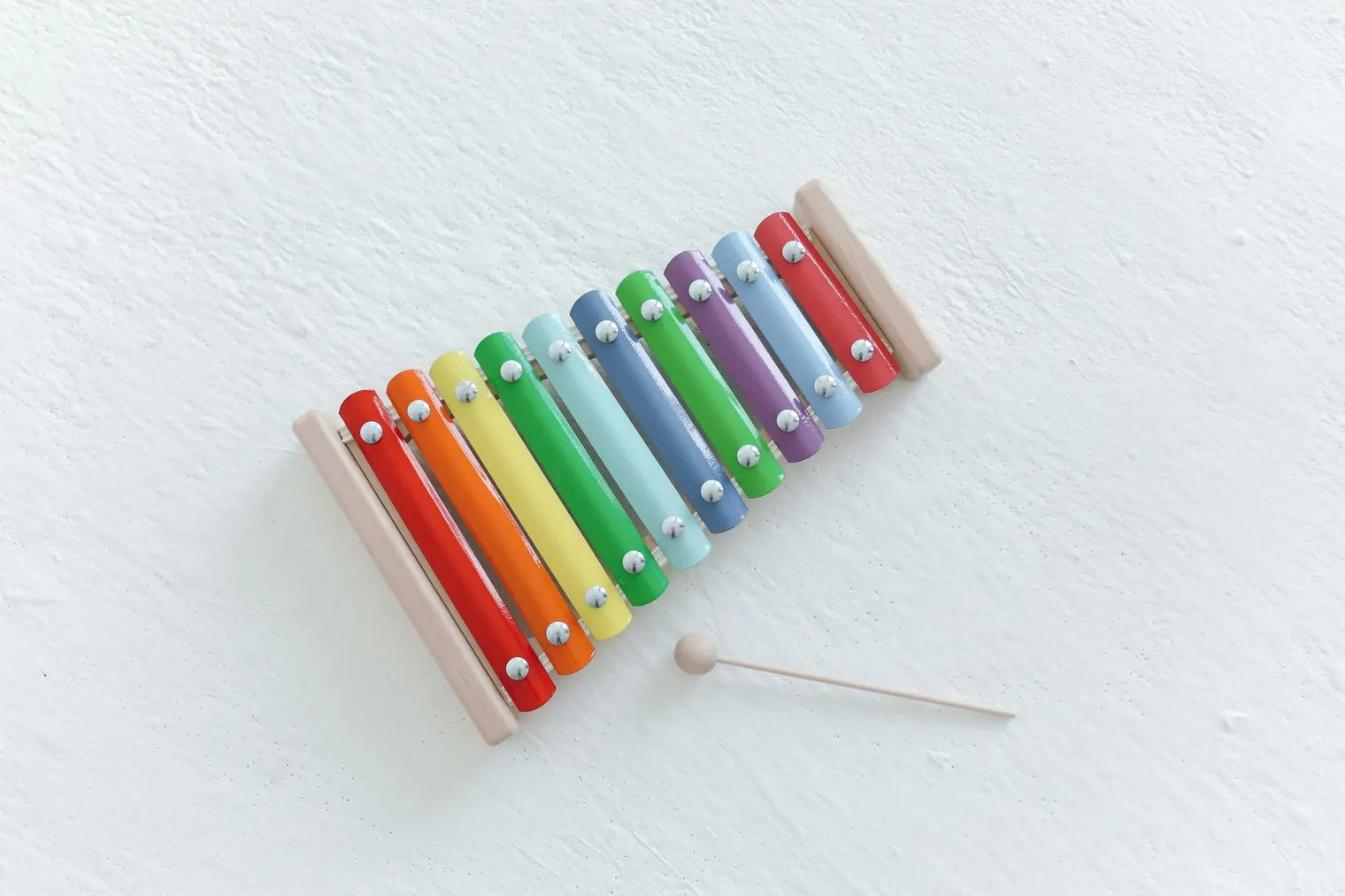 A rainbow-colored toy xylophone and its mallet on a white floor